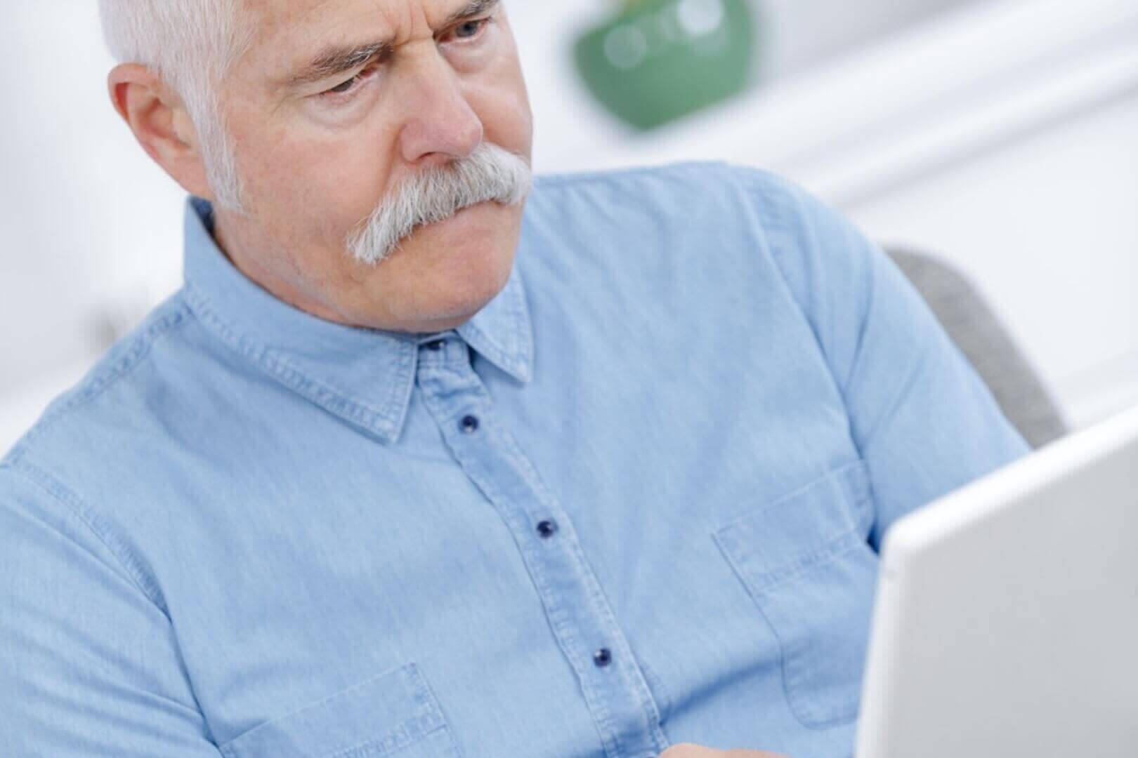 Elderly man engaged in virtual counseling session on laptop, wearing a blue shirt.