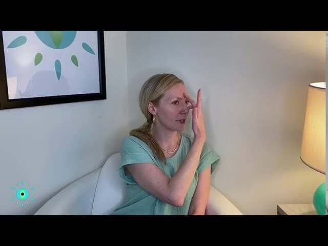 Woman practicing EFT tapping technique in cozy room with wall art and lamp.